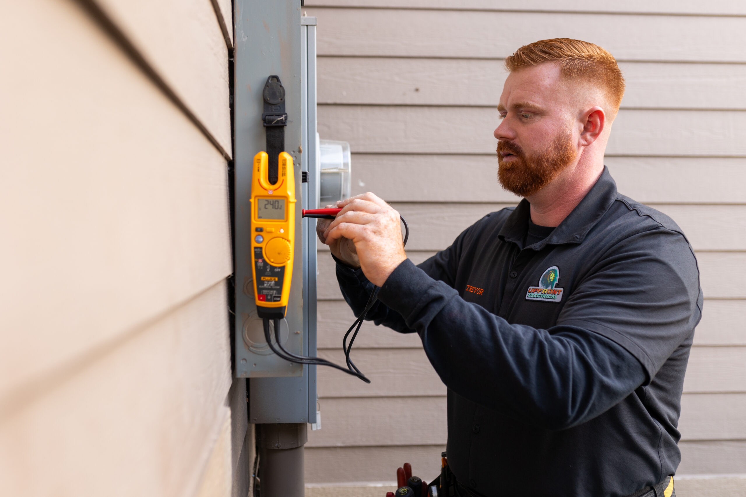 A technician uses a digital multimeter to check an electrical panel mounted on the exterior of a building.